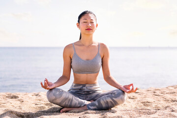 Fototapeta na wymiar young asian woman doing meditation at beach sitting with legs crossed, concept of mental relaxation and healthy lifestyle