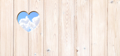 Heart-shaped hole in wooden boards and blue sky with clouds. Heart shape hole in wood fence. Go...