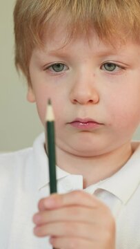Serious toddler boy studies green crayon pencil in hands