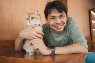 asian man smile and happy during play with his gold british cat in coffee shop