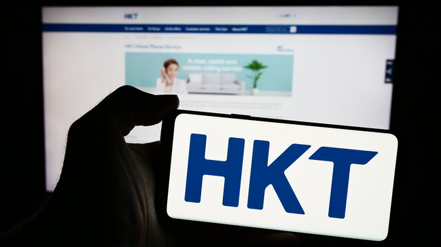 Stuttgart, Germany - 04-13-2024: Person holding mobile phone with logo of telecommunications company HKT Limited (Hong Kong Telecom) in front of web page. Focus on phone display.