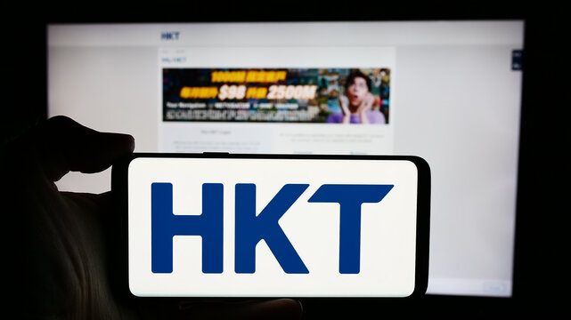 Stuttgart, Germany - 04-13-2024: Person holding cellphone with logo of telecommunications company HKT Limited (Hong Kong Telecom) in front of webpage. Focus on phone display.