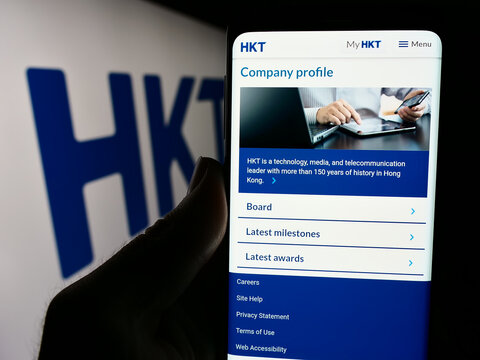 Stuttgart, Germany - 04-13-2024: Person holding smartphone with webpage of telecommunications company HKT Limited (Hong Kong Telecom) with logo. Focus on center of phone display.