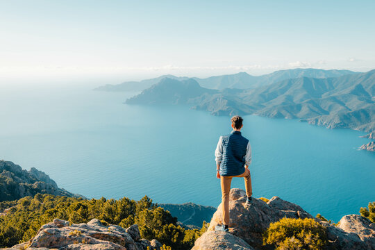 Man admiring the view of mountains and sea in Corsica. Sunset over calanques de Piana. Success and travel symbol