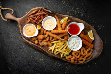 A large plateful of different kinds of potatoes: balls, slices, sticks with different sauces. Menu for a pub on a dark background. Colorful juicy food photography.