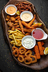 A large plateful of different kinds of potatoes: balls, slices, sticks with different sauces. Menu for a pub on a dark background. Colorful juicy food photography.