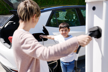 A mother guides her son in using an EV charger, forging a sustainable future.