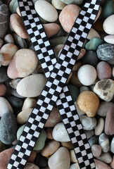 Crossed Black And White Plaid Ribbon On Smooth Sea Stones. Concept Photo For Illustration Competition Finish Flag  
