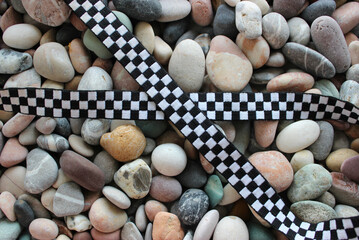 Racing Concept Design Stock Photo. Checkered Ribbon In Cross Form On A Colored Pebbles 
