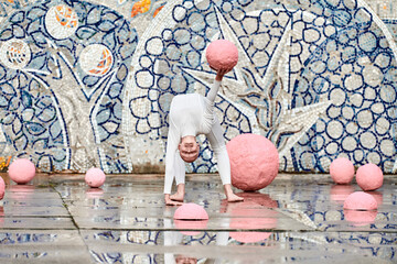 Outdoor dance of young ballerina girl with alopecia in white futuristic suit with plastic and flexible movements among pink spheres on abstract mosaic Soviet background, symbolizes self expression