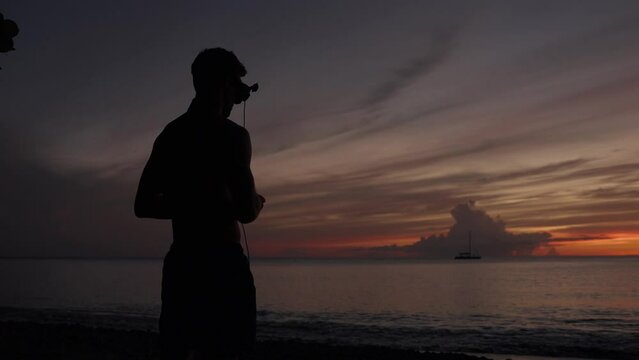 Silhouette of a man flying an fpv drone with goggles on at a beach on Saint Lucia at sunset.
