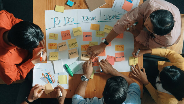Top view of people writing and making scrum task board while writing marketing and planning strategy at colorful sticky notes. Smart team manage work performance by using kanaban board. Convocation.