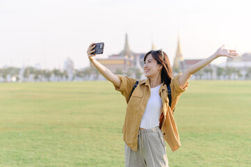 Traveler asian woman in her 30s making a livestream or selfie on smartphone while explores Wat Phra Kaew emerald Buddha. Share the wonders of Thai heritage through her journey. - 792476834