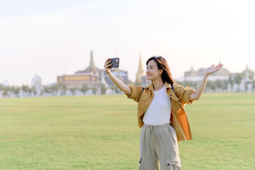 Traveler asian woman in her 30s making a livestream or selfie on smartphone while explores Wat Phra Kaew emerald Buddha. Share the wonders of Thai heritage through her journey. - 792476875
