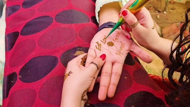 Indian woman using henna tattoo mehandi to write eat love travel repeat on the hand of the groom during the hindu wedding ceremony where these designs are traditional