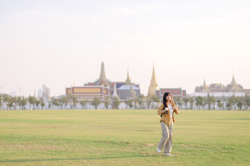 Traveler asian woman in her 30s, backpack slung over her shoulder, explores Wat Pra Kaew with childlike wonder. Sunlight dances on the golden rooftops, and a carefree smile - 792478009