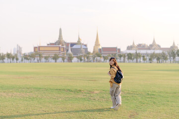 Traveler asian woman in her 30s, backpack slung over her shoulder, explores Wat Pra Kaew with childlike wonder. Sunlight dances on the golden rooftops, and a carefree smile - 792478040