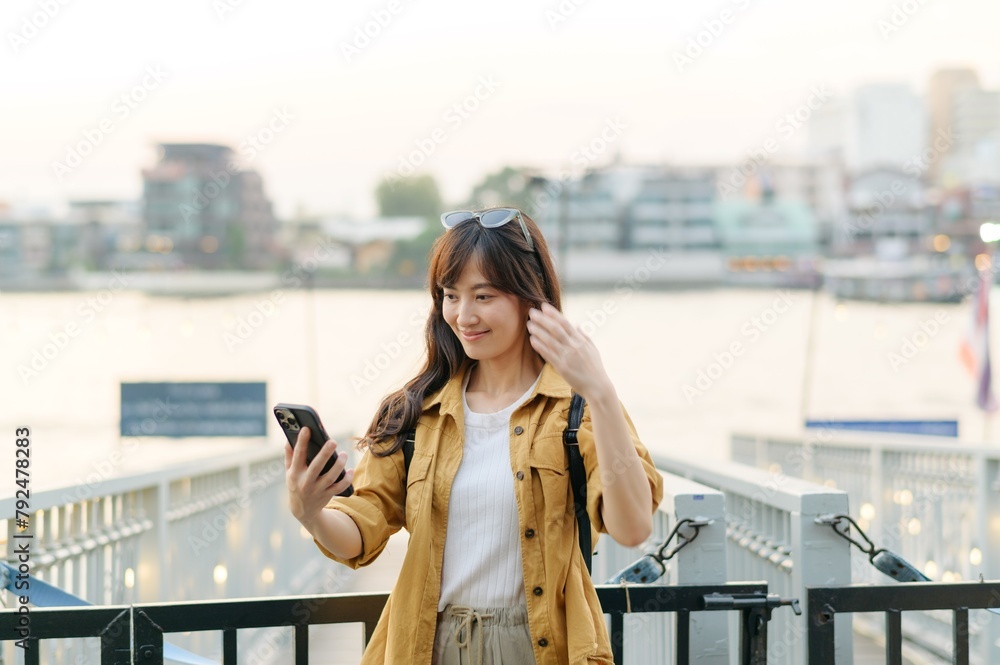 Wall mural young Asian woman in 30s on a solo adventure. Technology in hand, she captures the essence of cultural exploration and joyful discovery.