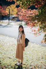 Casual dress elegance, Asian woman explores Kyoto's fall beauty, capturing cheerful smiles amid vibrant foliage and the scenic charm of Japanese tradition during a holiday.