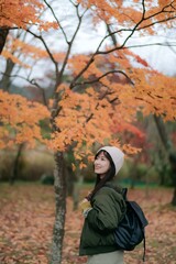 Asian woman in a lovely dress smiles amid the golden foliage. A pretty and cheerful portrait capturing the beauty of fall.