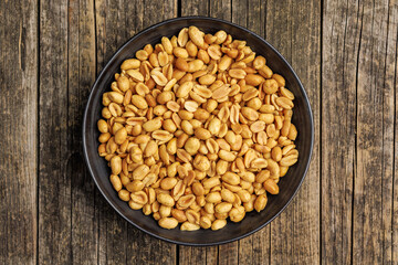 Salted roasted peanuts on  plate on wooden table. Top view. - 792478664
