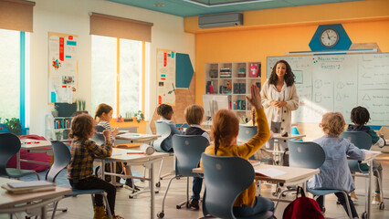 Caring Teacher Explaining a Math Lesson to a Classroom Full of Bright Diverse Children. Little Girl Raising Her Hand and Asking Tutor a Question. Primary School with a Group of Smart Multiethnic Kids - obrazy, fototapety, plakaty