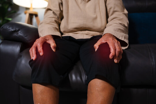 close up senior woman suffering from knee pain while sitting on sofa in living room at night