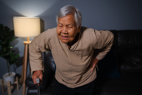 senior woman suffering from lower back pain in living room at night
