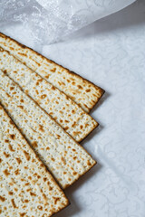 Pieces of matzo, a type of unleavened flatbread integral to Jewish Passover. The matzo is light brown with charred spots indicating its baked nature. The matzah is laid out on a white textured surface