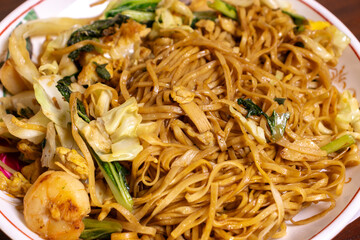 Fried noodle with chicken and vegetables in a white bowl on a wooden table. After edits.