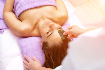 Relaxing massage. European woman getting quartz guache face massage in spa salon, side view