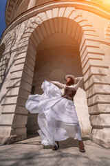 Stylish woman building city. A dancer in a long white skirt dances in front of a building with an arch. The skirt develops in the wind.