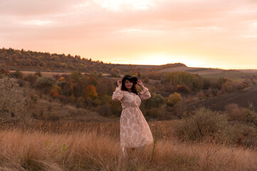 Woman in dress and hat in grass on the hill at evening	