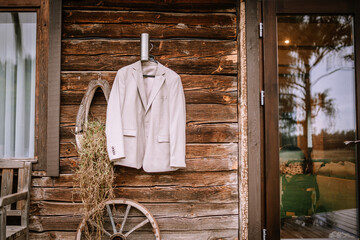 Valmiera, Latvia - August 10, 2023 - A light-colored suit jacket hangs on a rustic wooden wall next...