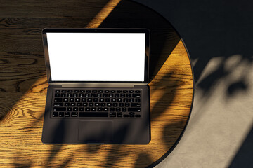 Top view of modern designer desktop with white mock up laptop on wooden desk, sunlight and shadows. 3D Rendering.