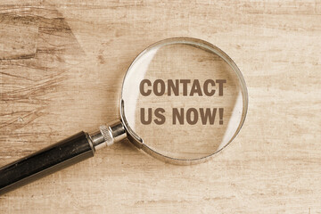 CONTACT US NOW word inscription visible through a magnifying glass on an old faded background - obrazy, fototapety, plakaty
