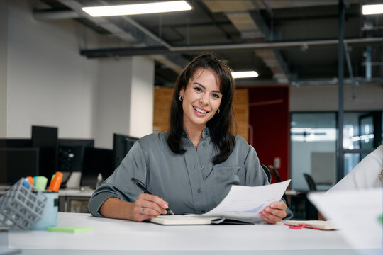 Two happy multiracial businesswomen smiling while reviewing documents during meeting in office