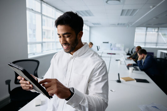 Happy young businessman in businesswear using digital tablet by desk in office