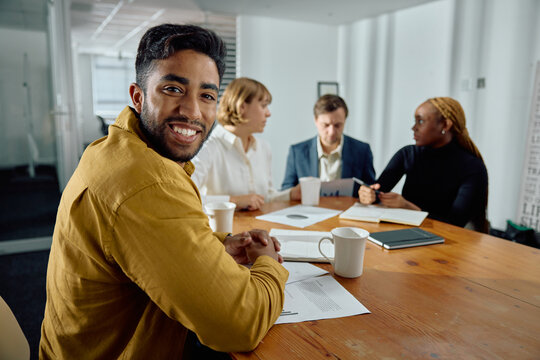 Four happy young multiracial adults in businesswear talking in meeting room at office