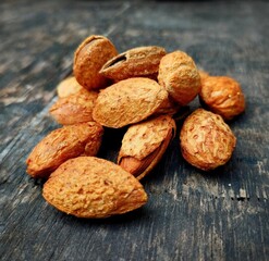 A pile of almonds on a wooden table. The almonds are brown and appear to be slightly dried out
