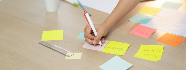 Closeup imaged of young creative businesswoman writes on colorful sticky note and places it on...