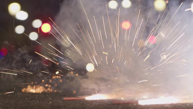 A close-up of a child's hand lighting a firecracker on the sidewalk in a night city, against a background of bokeh-style lanterns. Valencia, Spain, Las Fallas celebration