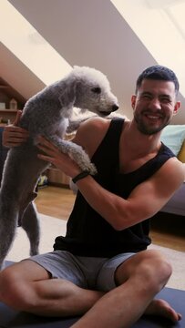 A man sits on a yoga mat, holding a dog in his arms for comfort