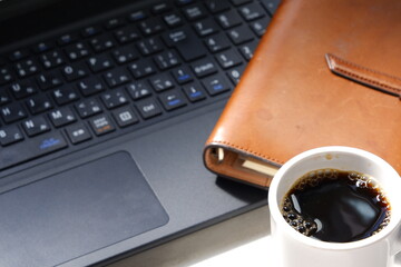 コーヒーを飲みながら、ノートパソコンとシステム手帳でデスクワークをしているイメージ