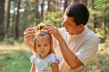 Dad and daughter with funny ponytail smiling in park happiness or love in summer sunshine young family baby girl walking together dad straightens his daughter's hairstyle