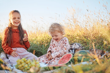 Funny little kids eating watermelon on green grass on nature at summer day. Brother and sister outdoors. Toddler Boy and Baby Girl. Children eat fruit at garden. Childhood, Family, Healthy Eating.
