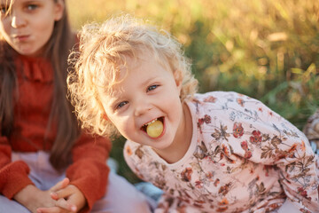Happy Caucasian little girls sisters playing together in the summer outdoors having picnic eating fruits expressing happiness having fun together on sunny summer day