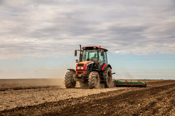 Powerful tractor at work, turning over soil on a vast farmland under a clear sky - obrazy, fototapety, plakaty