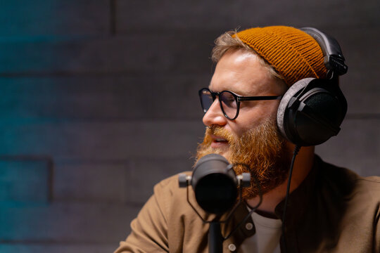 Man with facial hair and eyewear using microphone for recording podcast