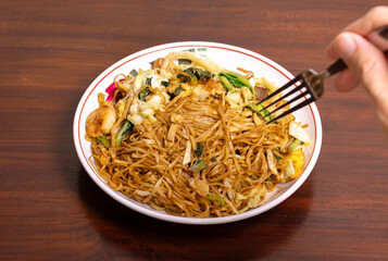 Fried noodle with chicken and vegetables in a white bowl on a wooden table. After edits.